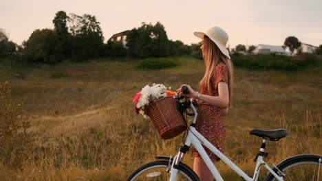 Side-view-of-smiling-sexy-blonde-girl-in-a-light-summer-dress-is-walking-with-a-Bicycle-in-the-summer-in-the-handlebar-basket-of-wildflowers-in-slow-motion